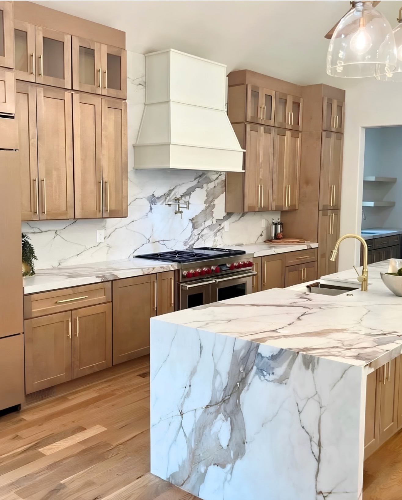 Warm wood kitchen with marble waterfall island and white range hood — St. Louis remodel by Phoenix Construction Group