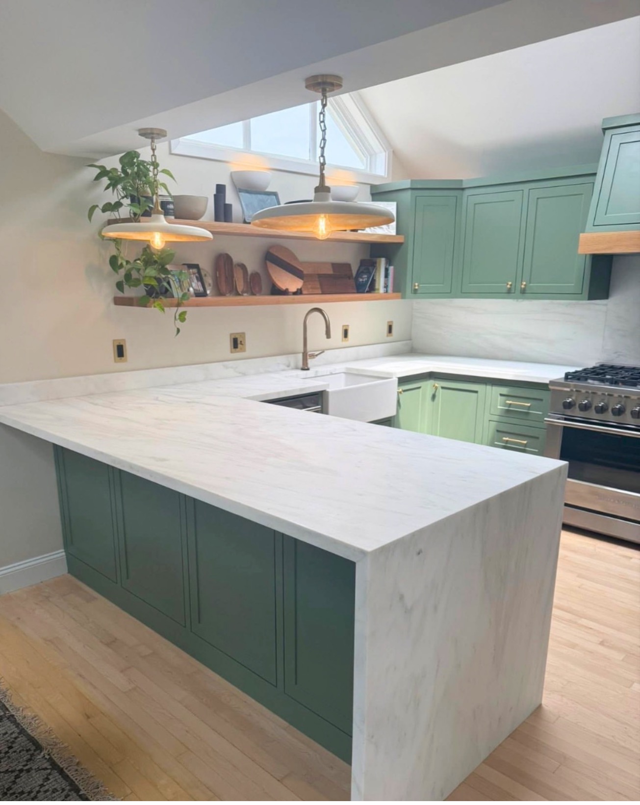 Bright sage green kitchen with marble peninsula, open shelves and farmhouse apron sink — St. Louis remodel by Phoenix Construction Group